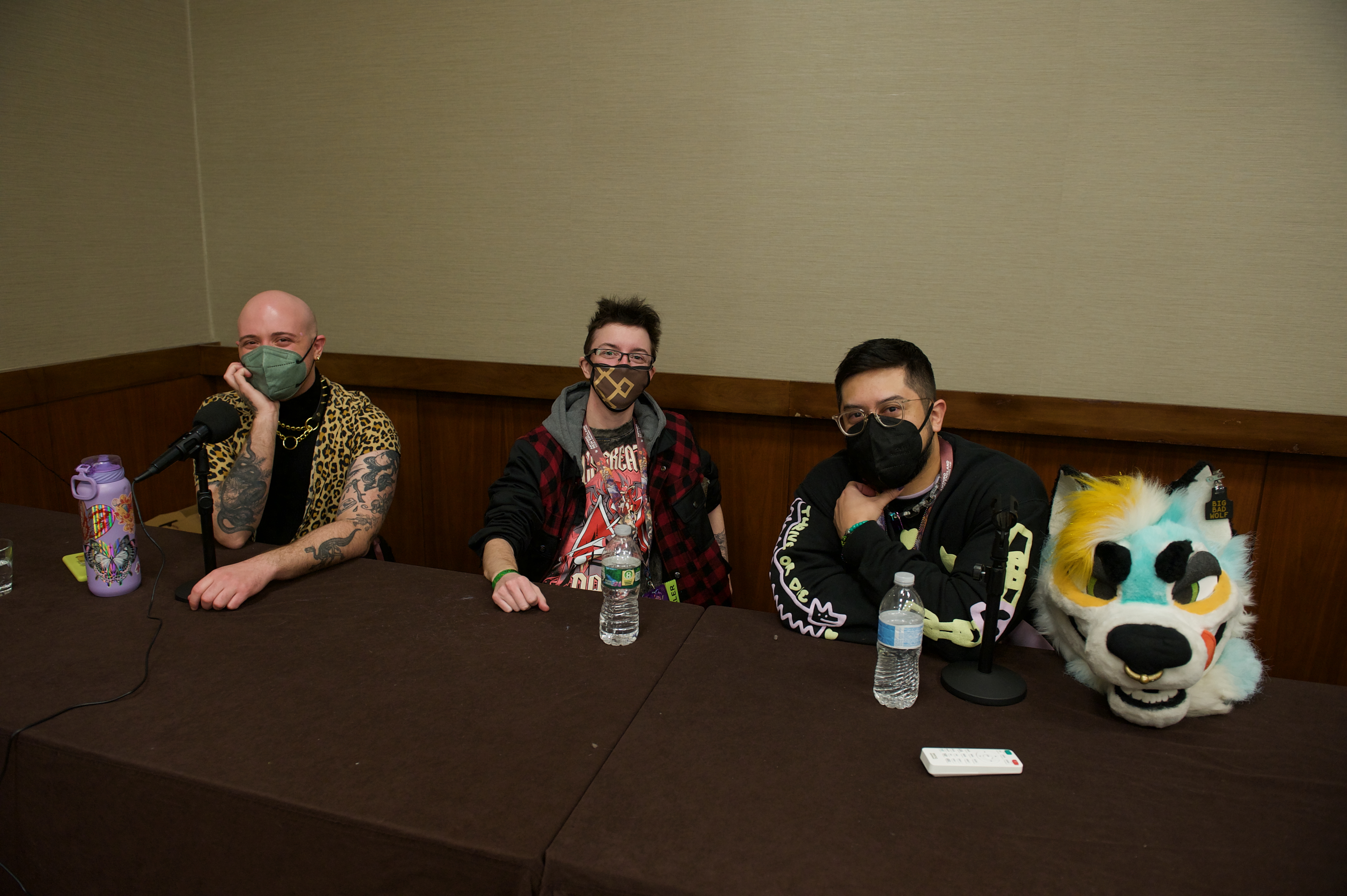 The three guests of honor sit at a long table, all wearing face masks.